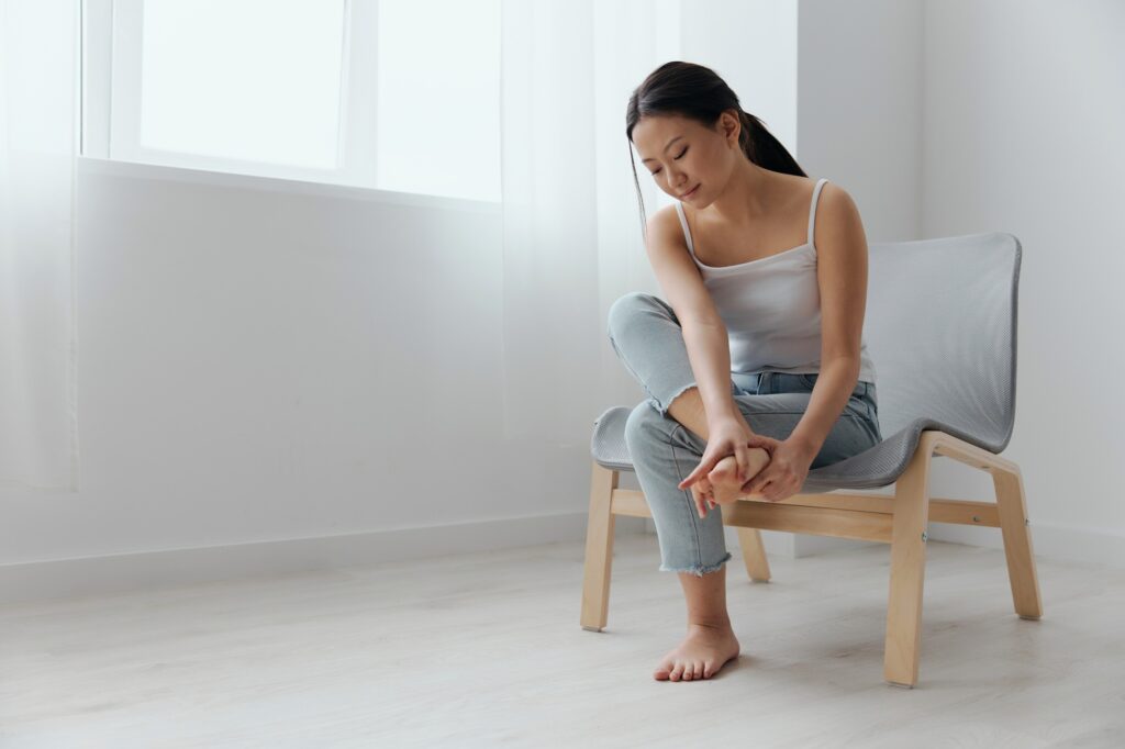 MLS Laser - Full body shot suffering tanned beautiful young Asian woman touch pain foot massaging feet at home