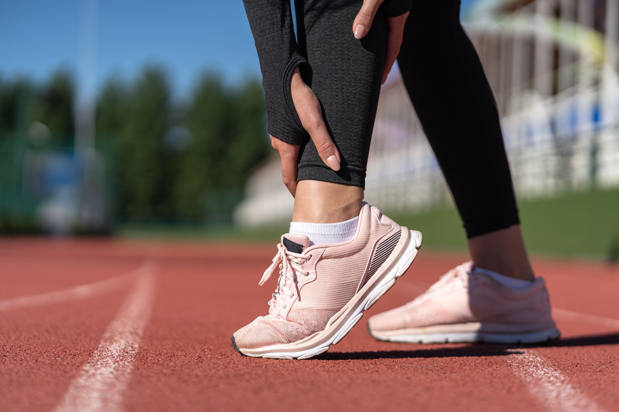 Sport Related Foot and Ankle Injuries - Jogger woman runner touching foot in pain due to sprained ankle. Running sport, injury from workout